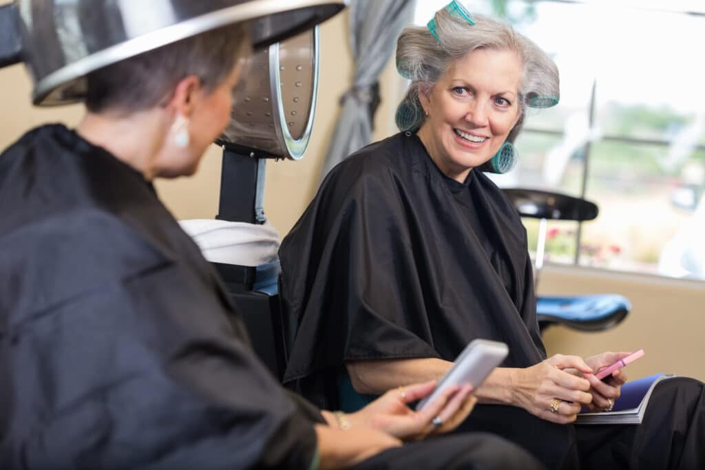 Senior women using smart phone during hairstyling appointment in salon