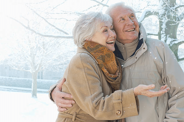 A senior couple standing outside in the winter snow smiling.
